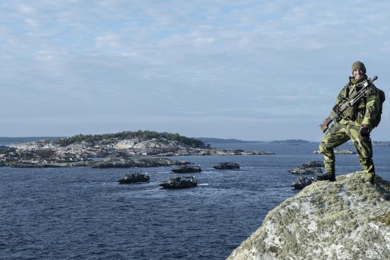 Amfibieskyttesoldat med stridsbåtar i bakgrunden.